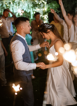 A couple is dancing at a festive event with sparklers in their hands, surrounded by people celebrating.