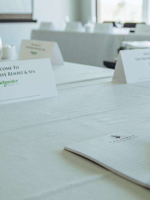 The image shows a conference room setup with notepads, pens, and glasses on a table, plus a sign reading 